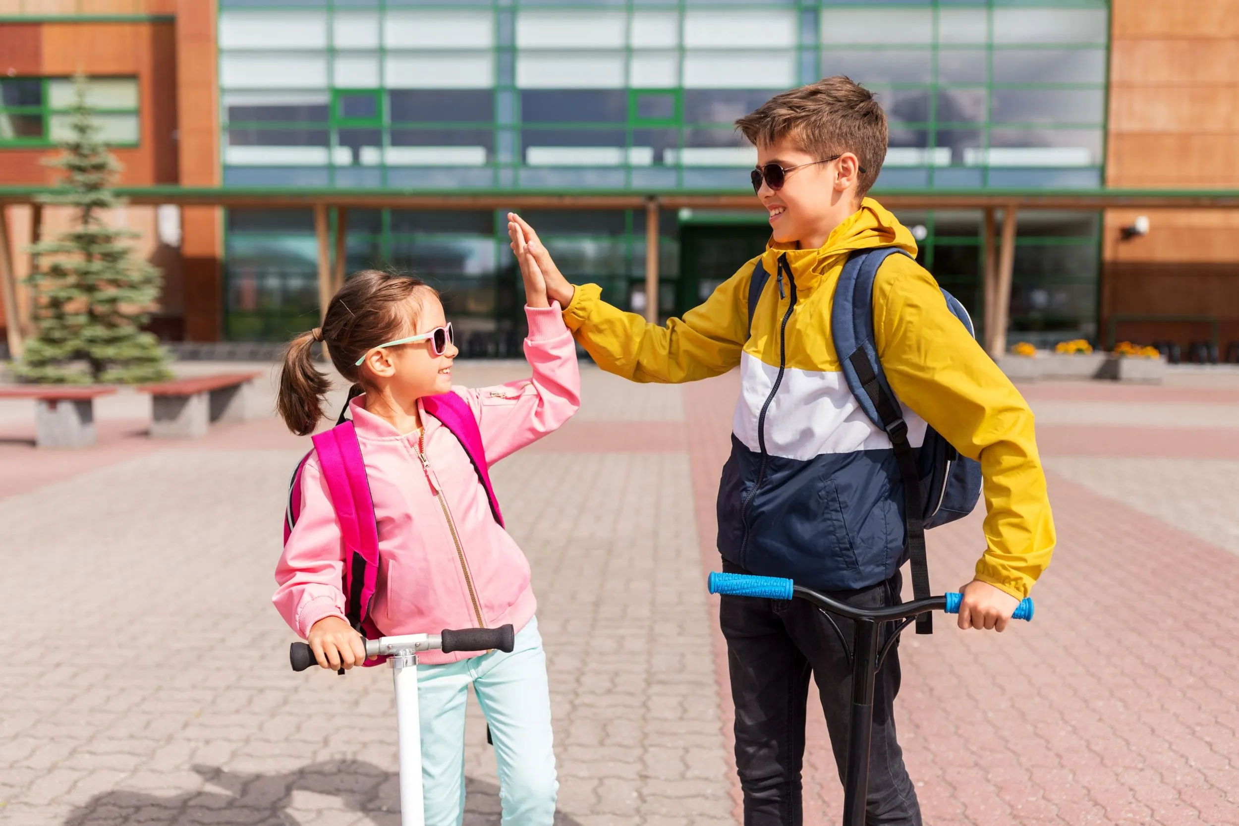Two children high-fiving outside their school, wearing backpacks